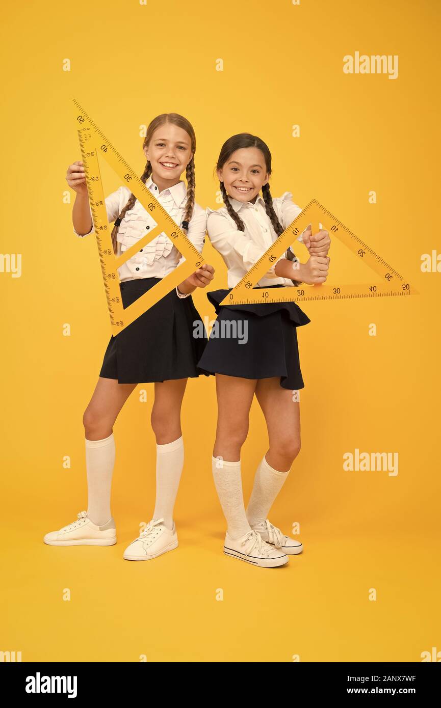 geometric shapes. pupils use gon ruler. stem disciplines. back to school. Maths and geometry. Kids in uniform at yellow wall. friendship and sisterhood. happy small girls study mathematics. Stock Photo