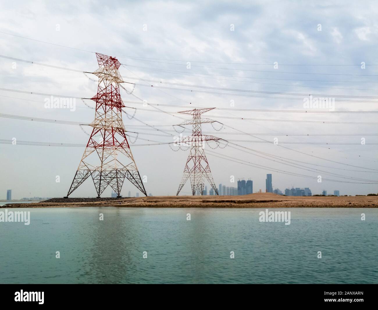 Red and white overhead electricity power lines and cables crossing water supported by large red and white pylons in Abu Dhabi, UAE Stock Photo