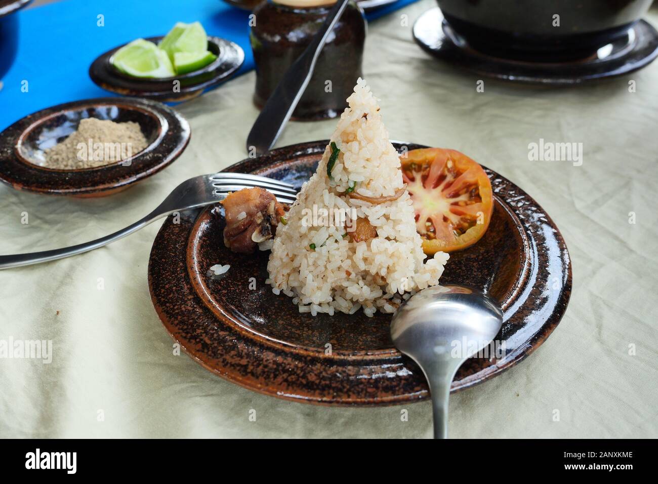 Zongzi or Traditional Chinese Sticky Rice Dumpling with sliced tomato with spoon and fork on brown dish, Chinese food with plate of pepper and lime Stock Photo