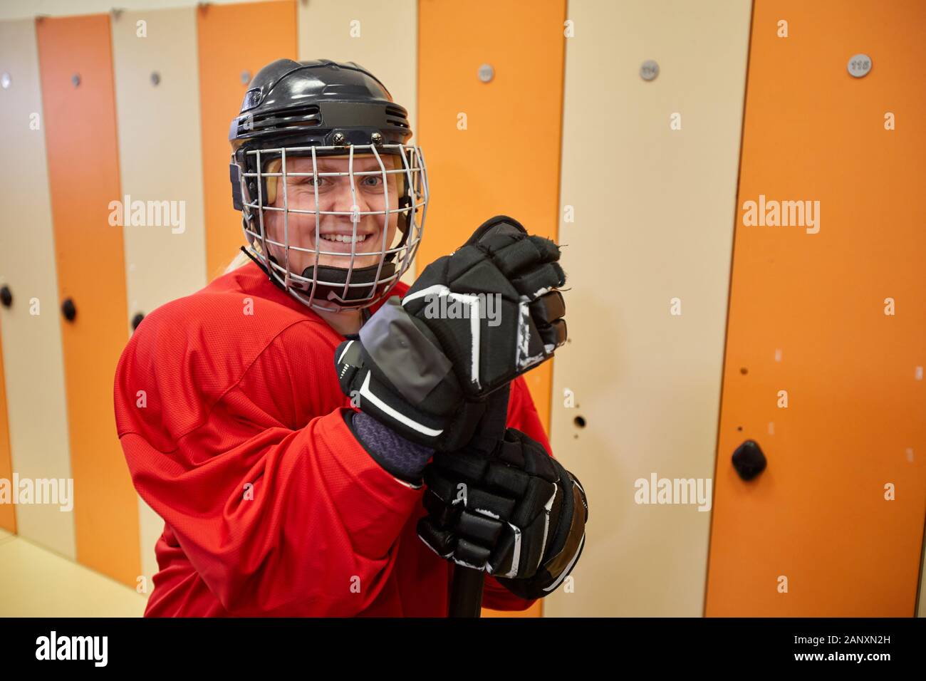 Waist up portrait of female hockey player wearing full gear smiling at