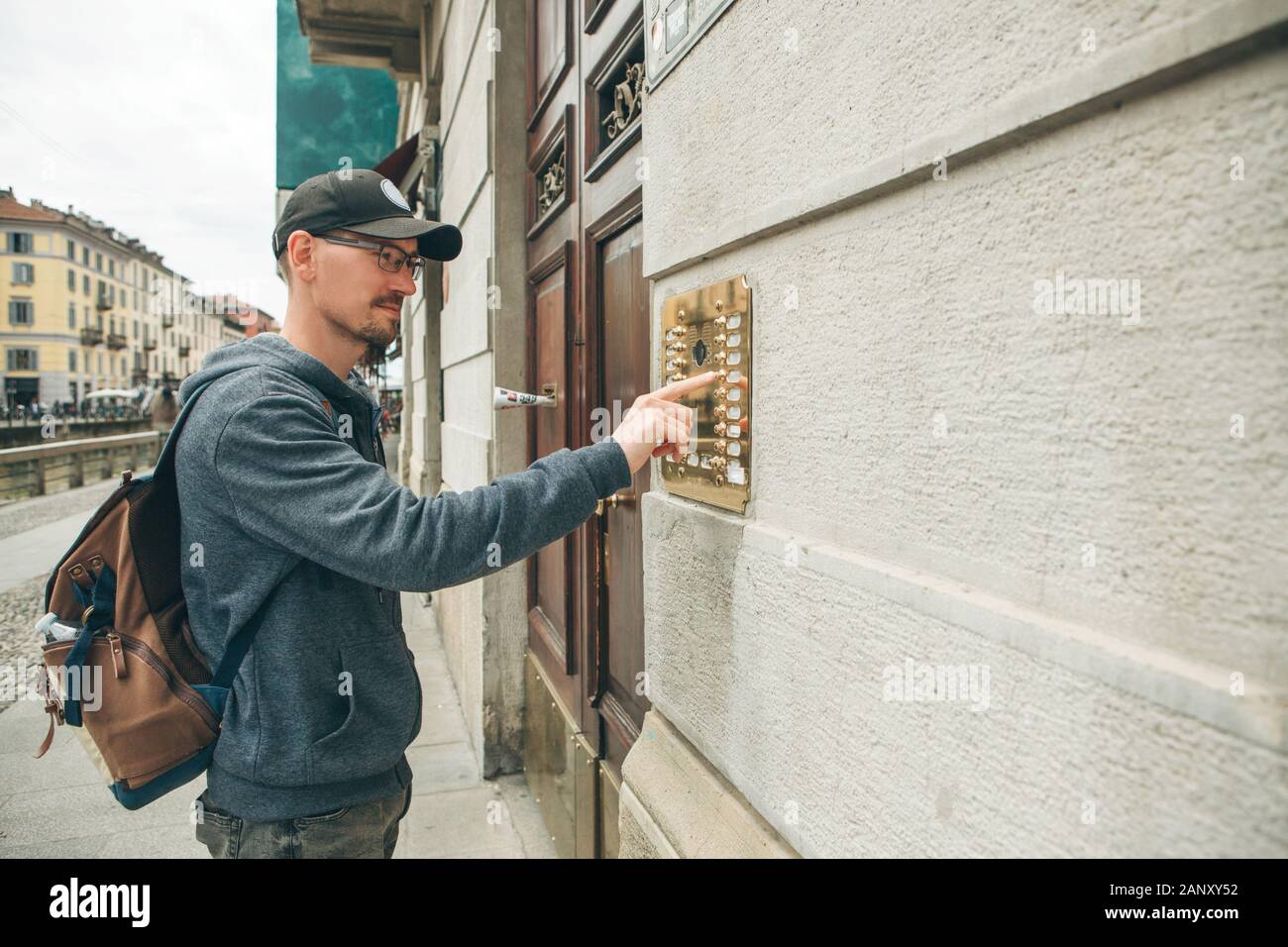 A guy or a man or a tourist presses a doorphone button to access inside. Stock Photo