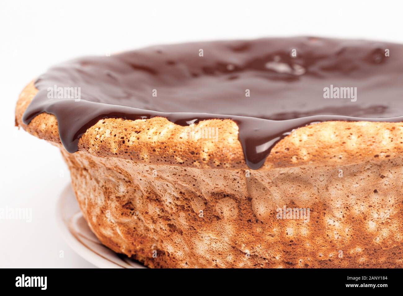 flowing chocolate on the sides of the cake. sponge cake with caramel pouring around the edges on white background close up. Stock Photo