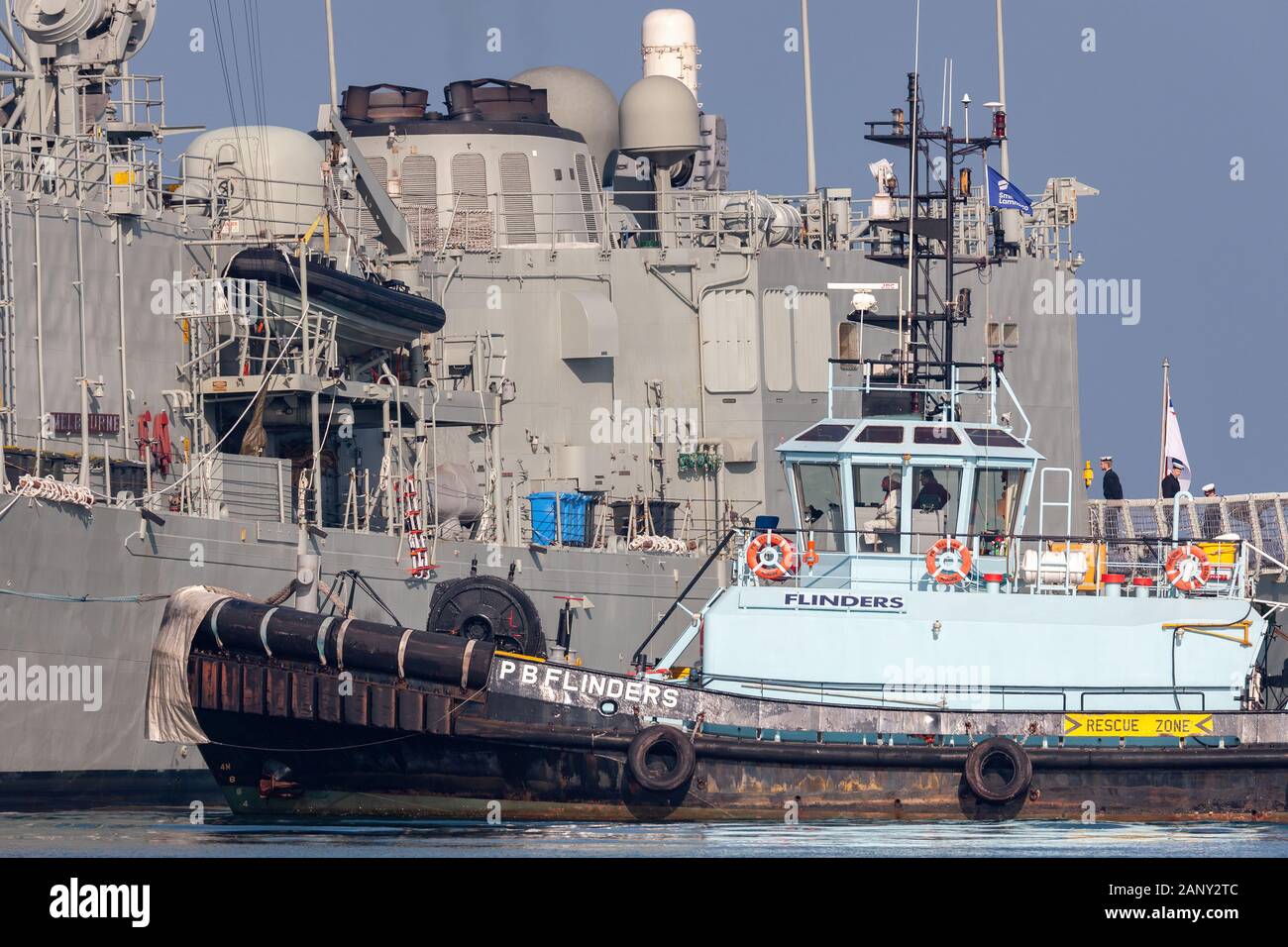 Tug boat PB Flinders assigning the HMAS Melbourne (FFG 05) guided-missile frigate of the Royal Australian Navy dock at Station Pier in Melbourne. Stock Photo