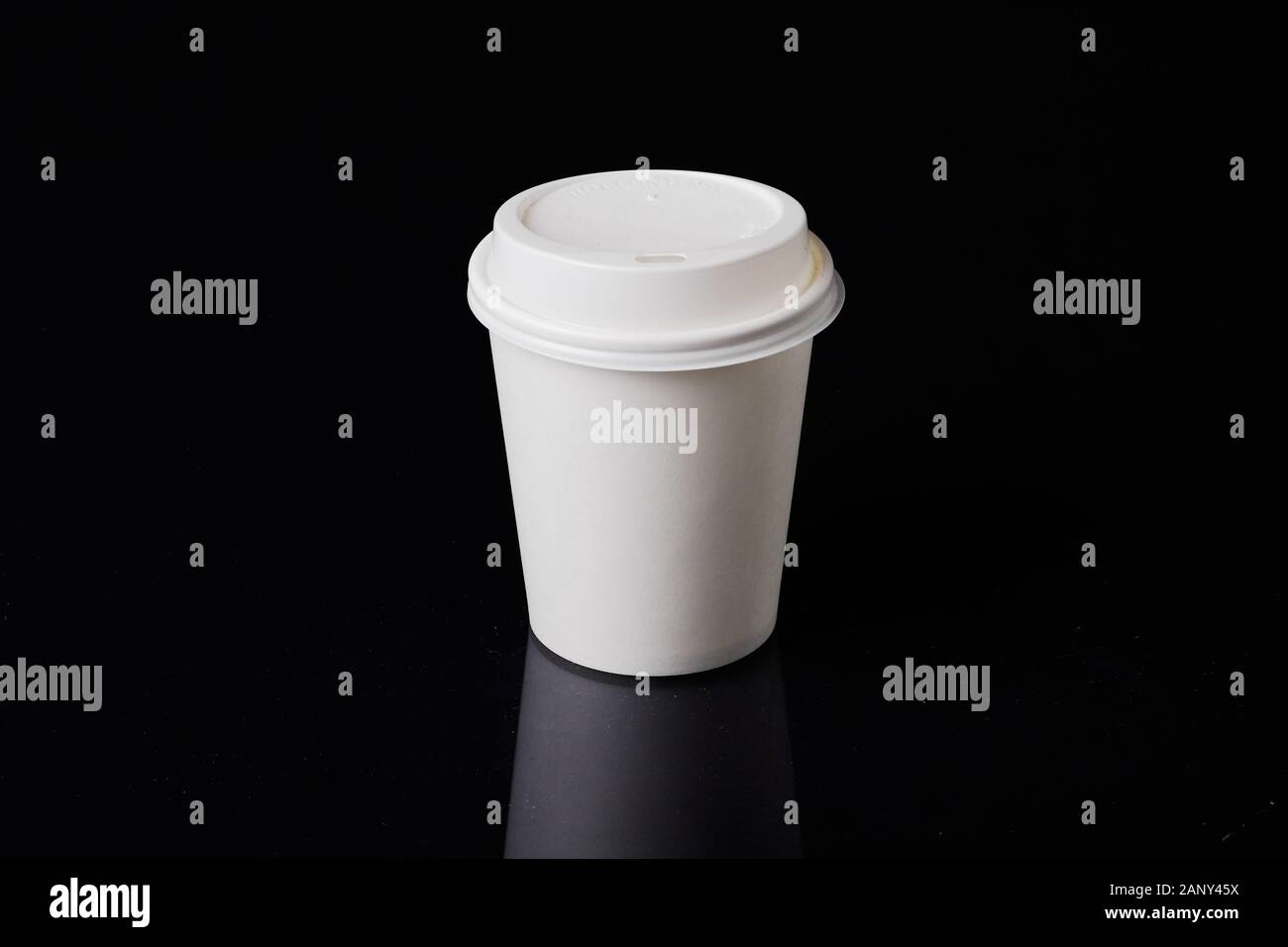 White disposable carboard coffee cup with plastic lid on a black background. Stock Photo