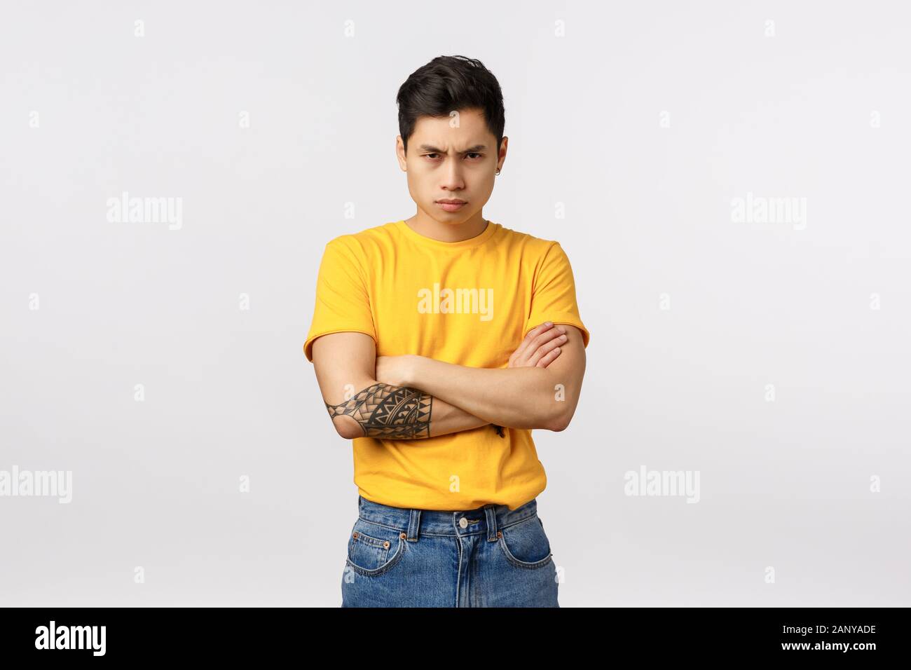 I am mad at you. Angry and displeased, offended defensive asian man in yellow t-shirt, cross arms over chest, frowning sulking and look from under Stock Photo
