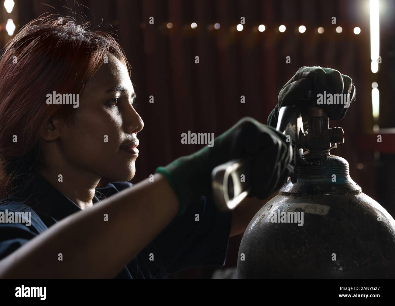 Female apprentice industrial engineer, inspecting and maintaining compressed gas cylinders in production plant - Trainee student intern, learning on the job skills during work experience Stock Photo
