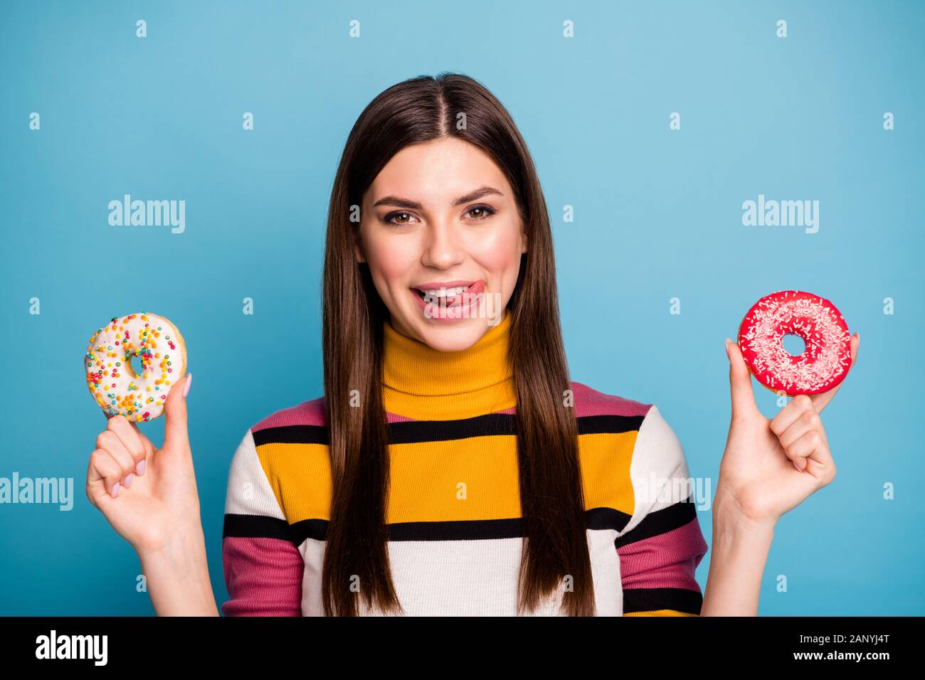 Close up photo of funky positive emotions girl hold two pastry sugary cookies lick lips want eat wear casual style jumper isolated over blue color Stock Photo