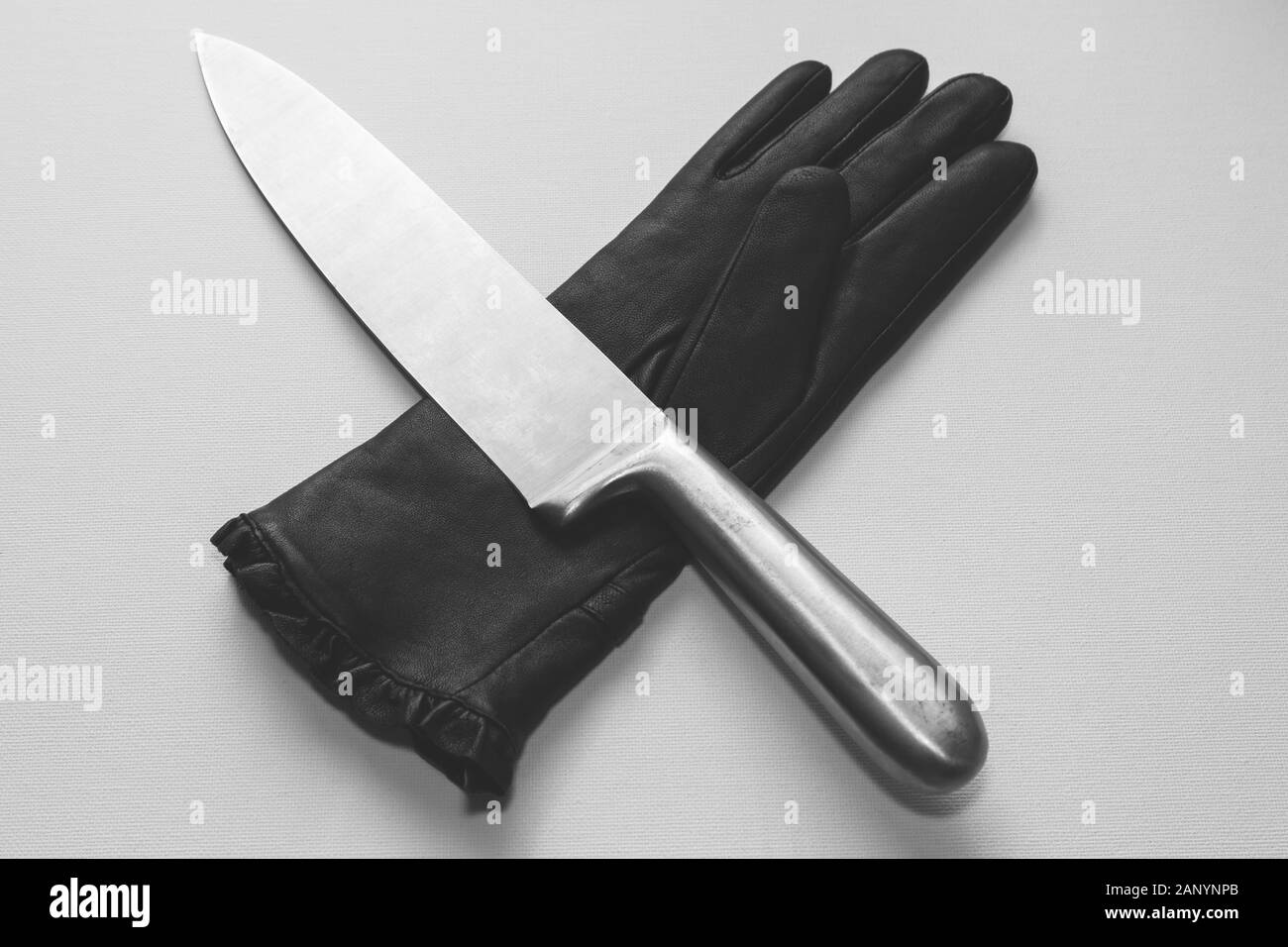 Overhead shot of a metal knife over a black glove on a white surface Stock Photo