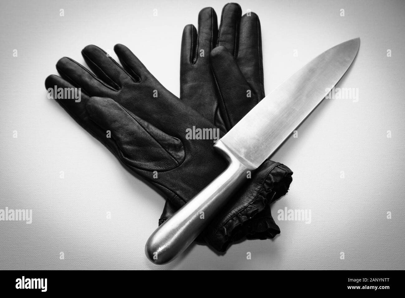 Overhead shot of a metal knife over black gloves on a  white surface Stock Photo