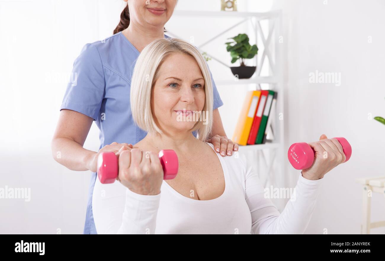Modern rehabilitation physiotherapy. A physiotherapist helps an middle aged woman recover from an injury through exercise with dumbbells. Stock Photo