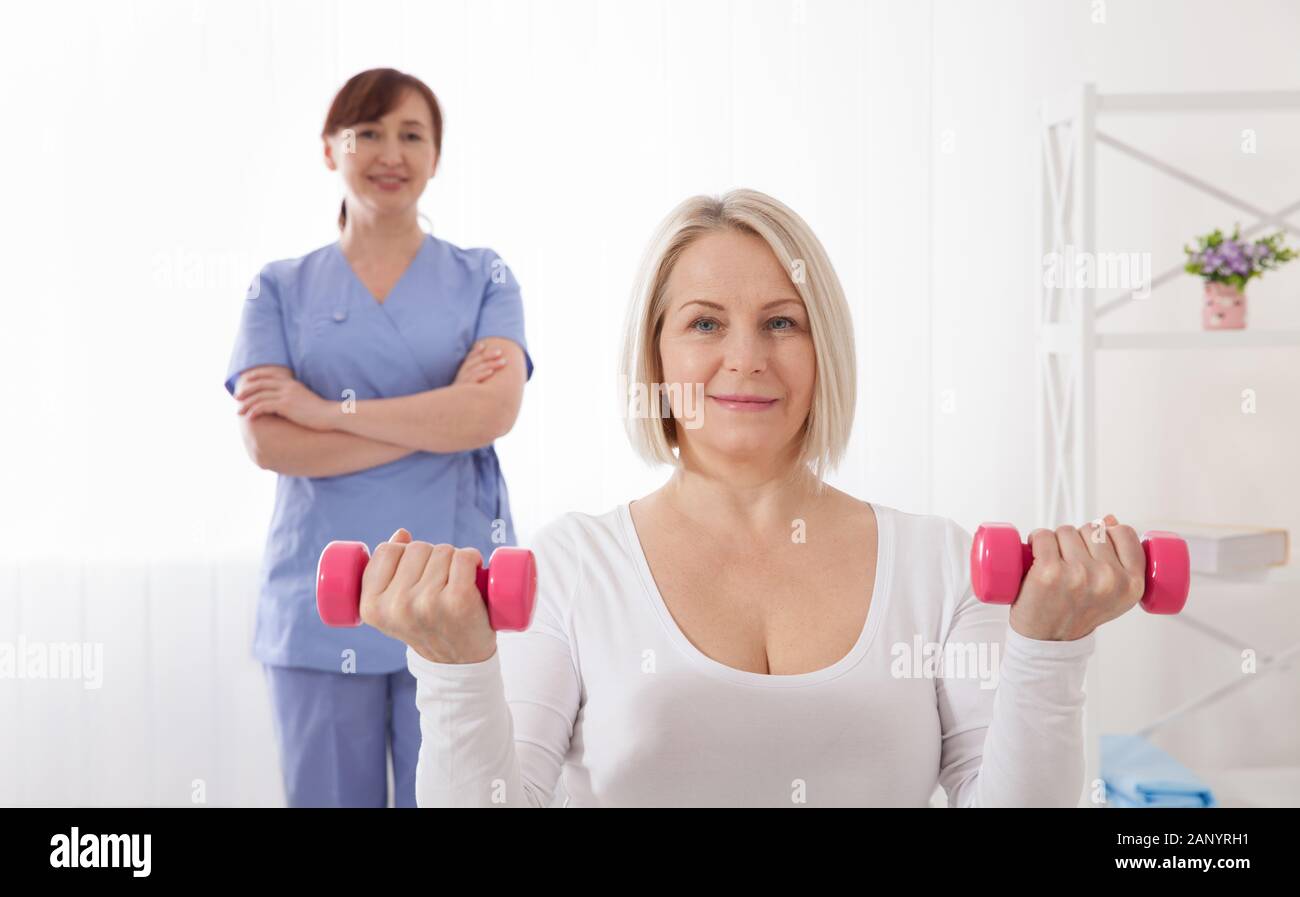 Picture of middle aged woman during rehabilitation in professional clinic. Rehabilitation, physiotherapy with dumbbells closeup. Stock Photo