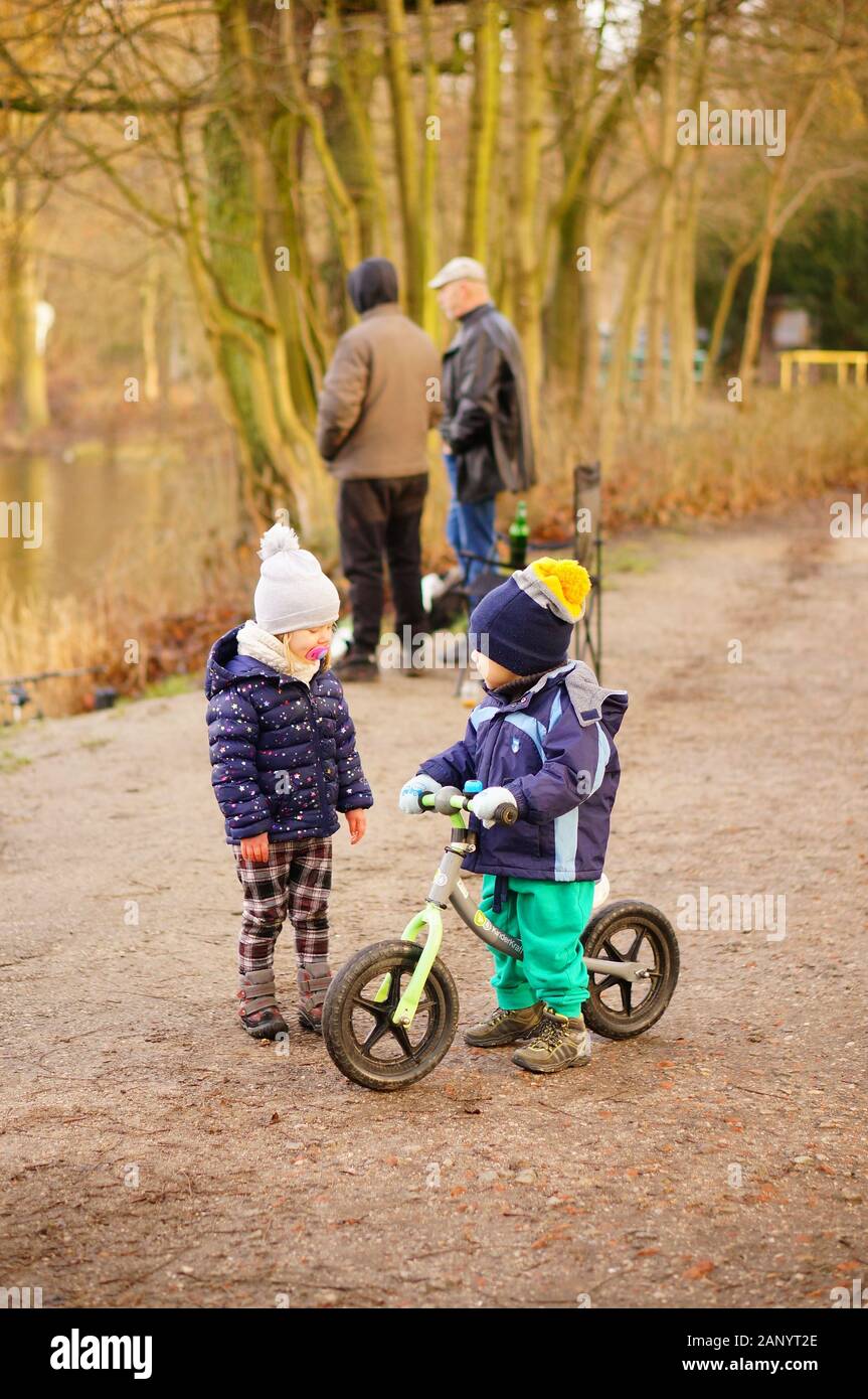 POZNAN, POLAND - Jan 12, 2020: Small boy on a bicycle and standing girl in the Debiec forest on a cold winter day. Stock Photo