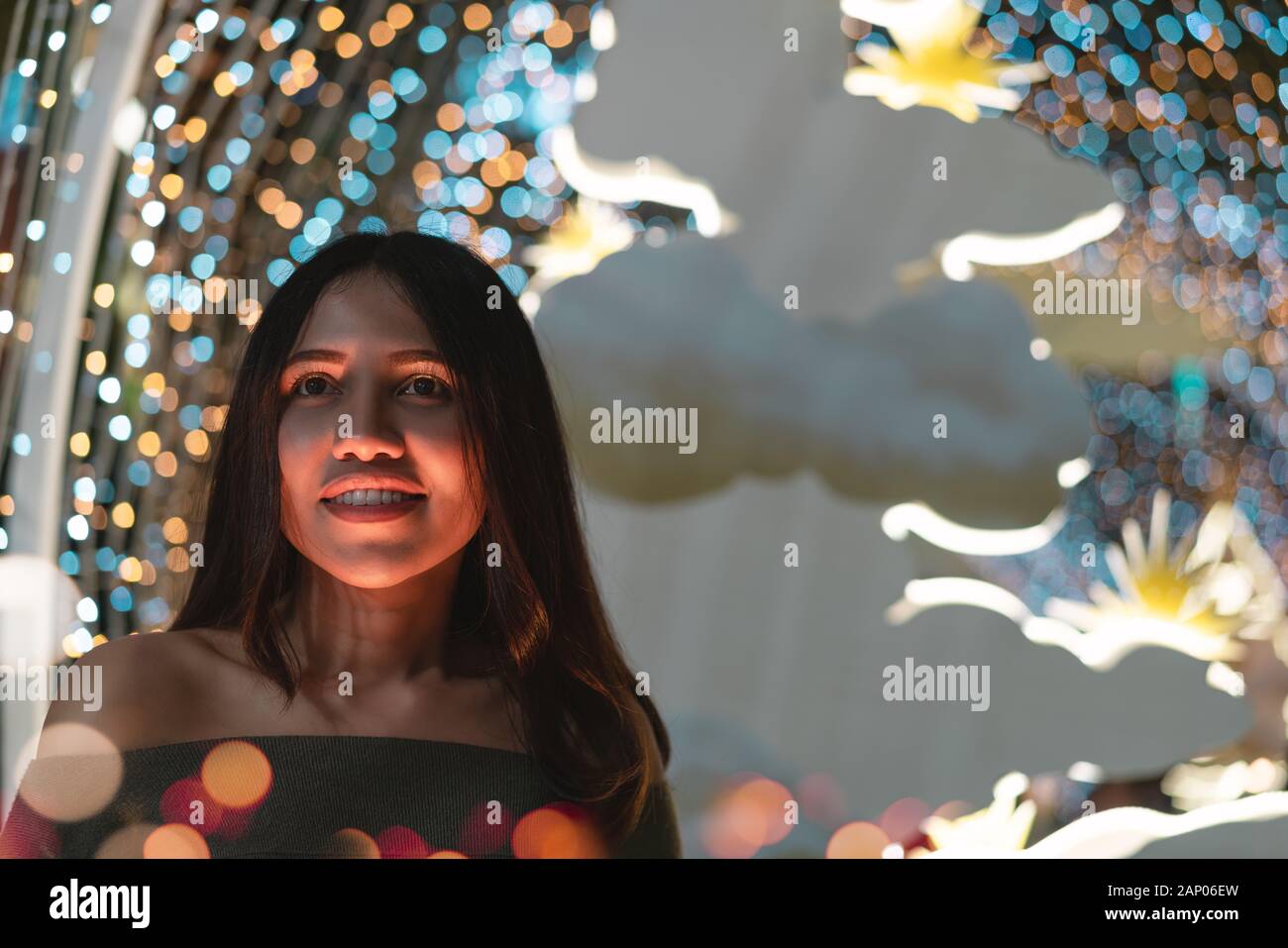 Young diverse woman smiling alone at night surrounded by colourful neon bokeh lights - Cute hipster American Asian girl with orange glow on face in club - Nightlife, dinner date and lifestyle concept Stock Photo