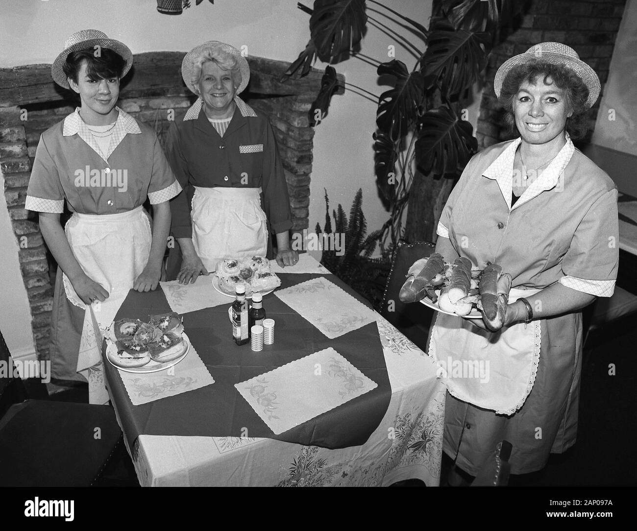 1980s, historical, three uniformed waitresses of different ages standing by a cloth covered table in a tea room, showing the rolls and open sandwiches available, Yorkshire, England, UK. Stock Photo