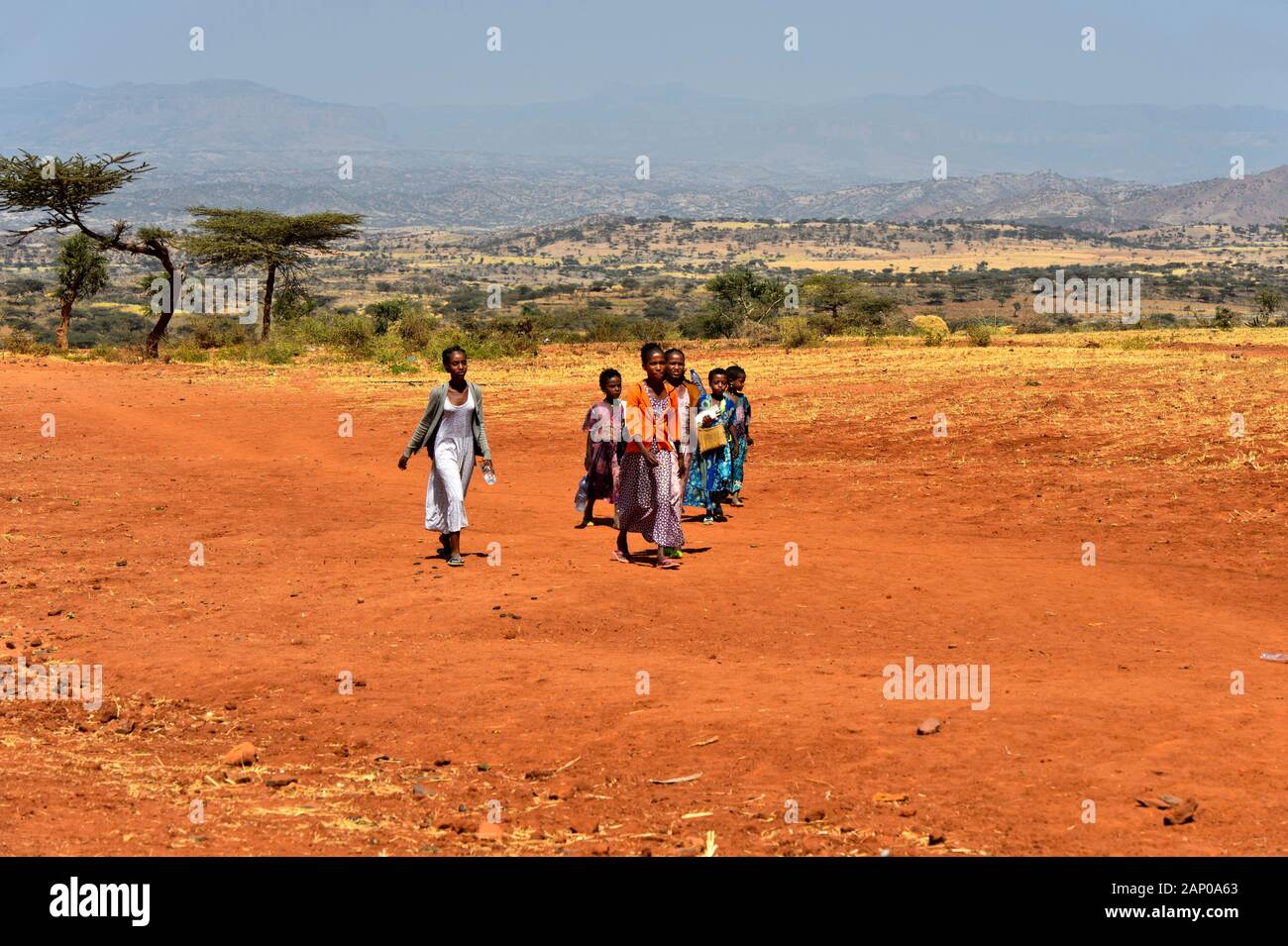 Group of young people walking across the rusty-red laterite soil of the Hawzien Plain near Hazwien, Gheralta region, Tigray, Ethiopia Stock Photo