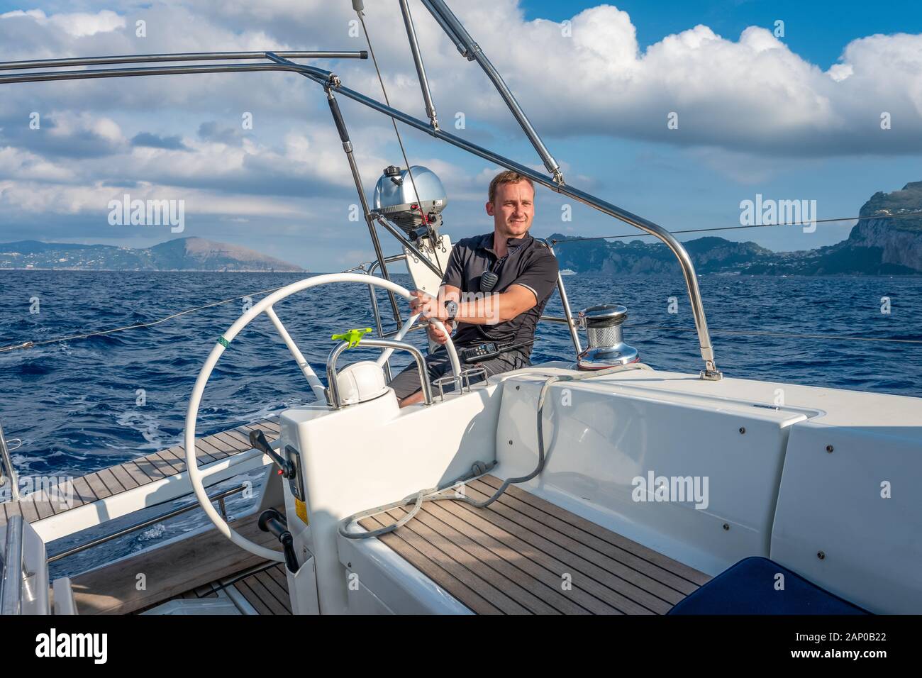 Sailor at the helm of modern sailing yacht. Mediterranean sea, near Ischia island and Capri island on the background, Italy. Stock Photo