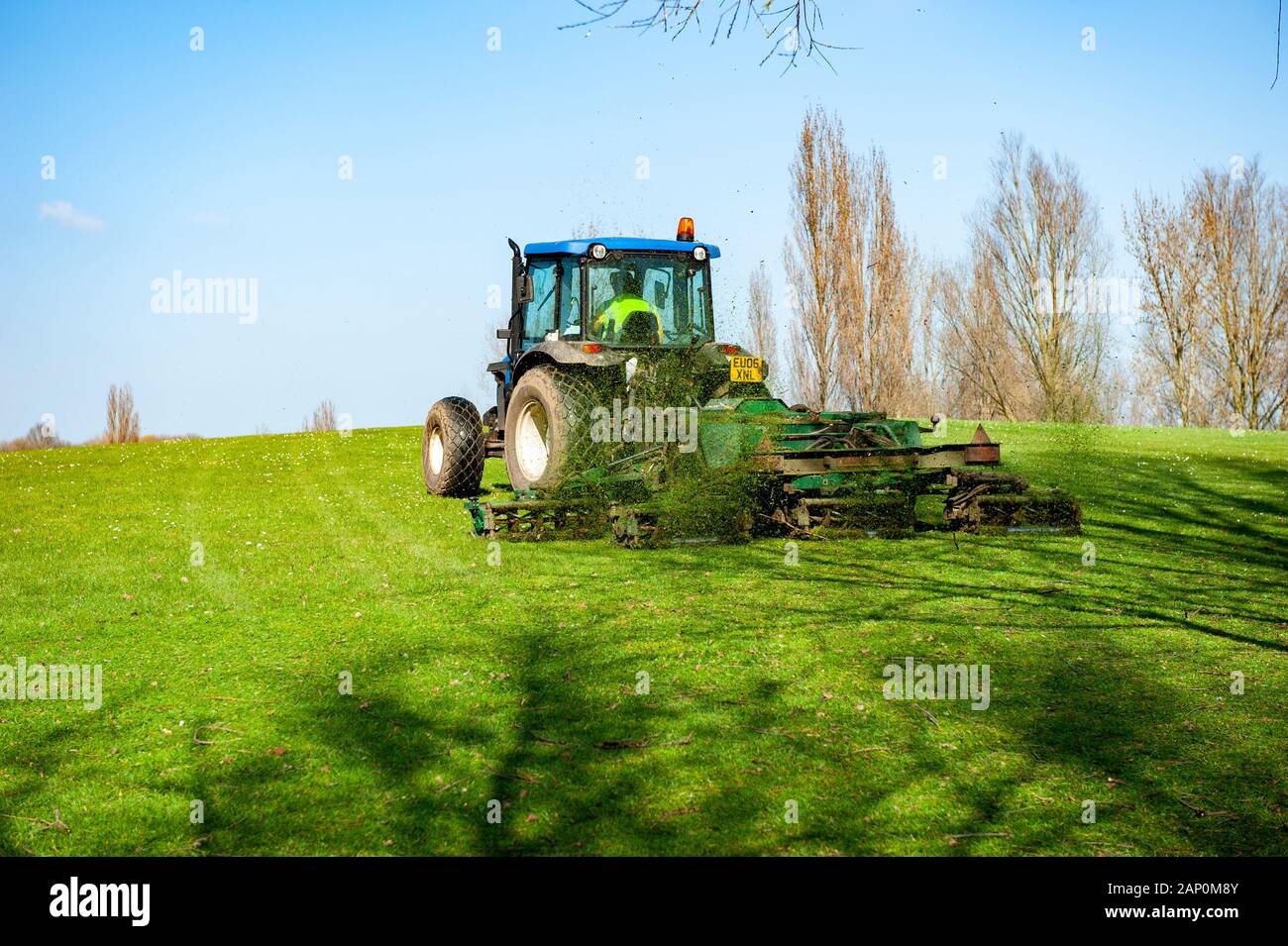 Council tractor with grass cutting attachment in use at a town park. Stock Photo