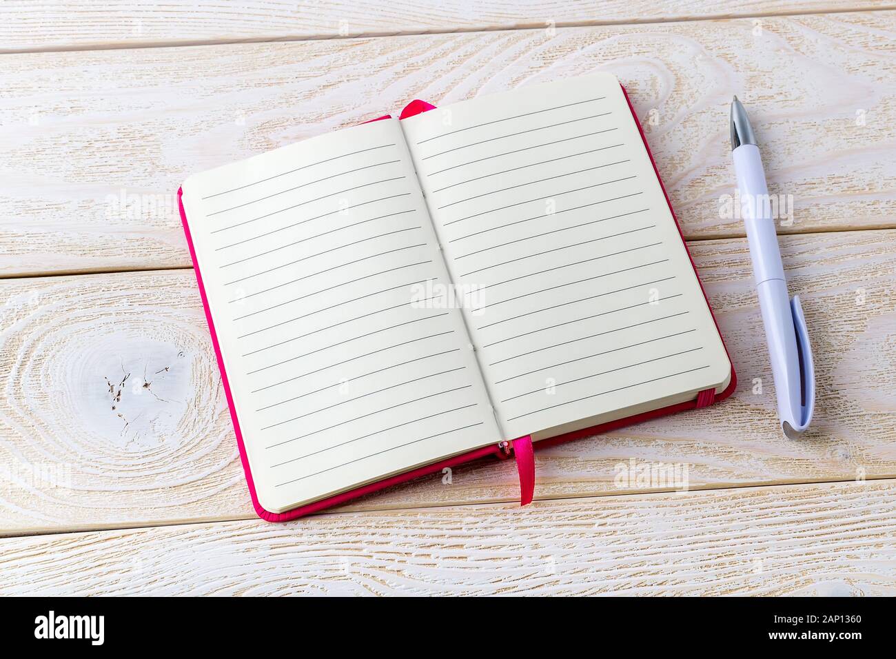 Opened lined paper notebook in a pink cover and white ballpoint pen on a white wood textured surface. Business, education and keep a diary concept. Stock Photo