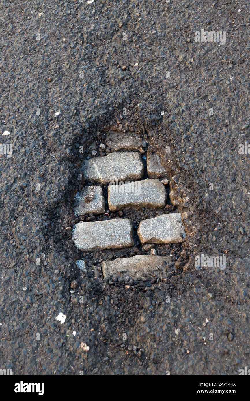 Pot hole on a tarmaced road exposes old cobblestones underneath Stock