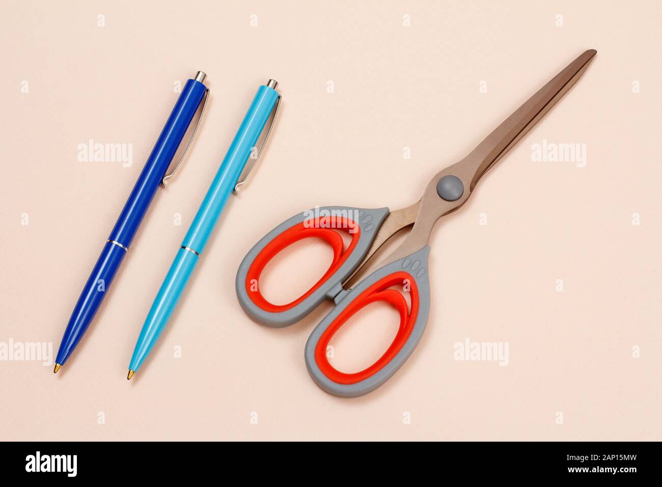 Two blue pens and scissors on a beige background. Top view. Stock Photo