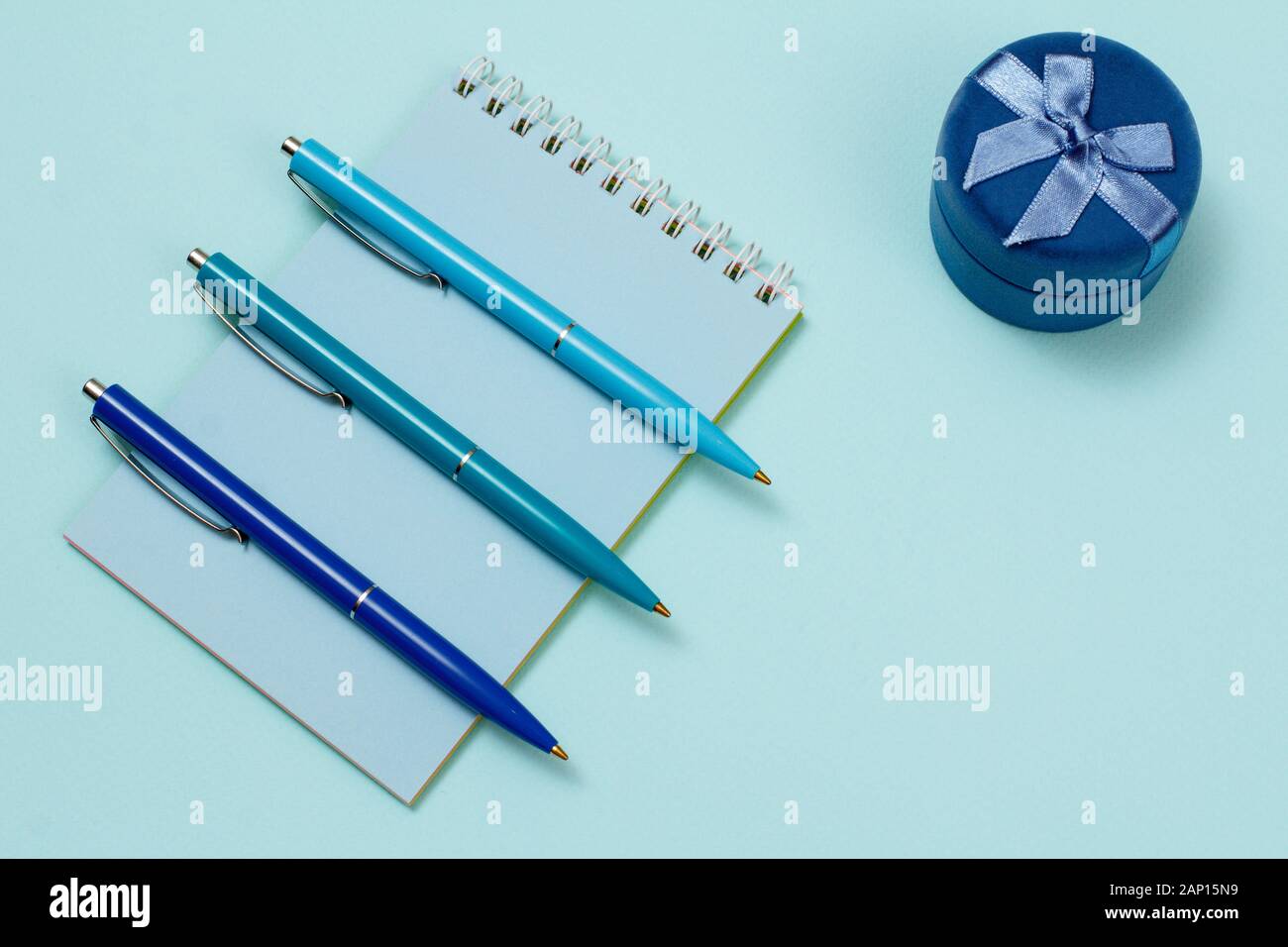 Three pens on a notebook and a gift box with a blue background. Top view. Stock Photo