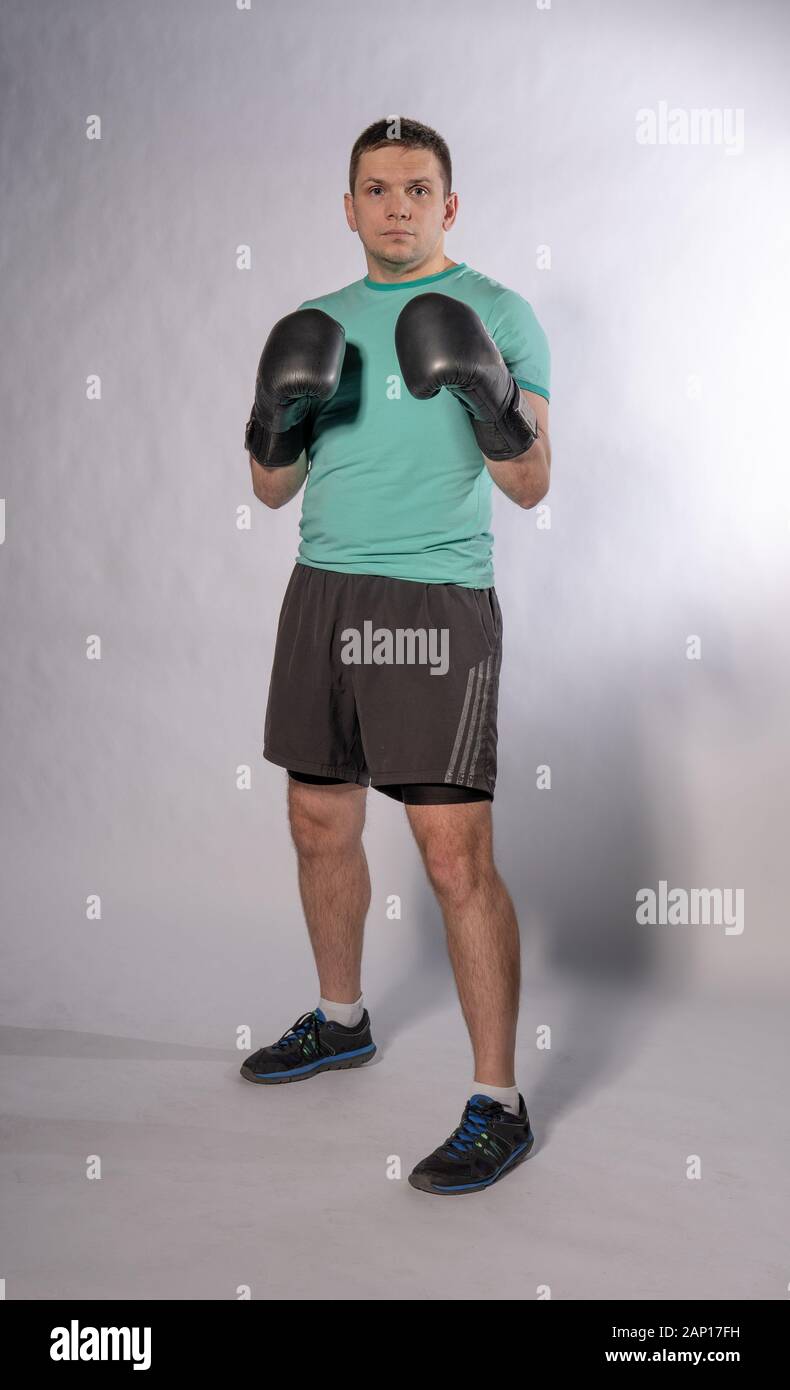 Professional boxer stands in black gloves with shorts in full-height background grey and white Stock Photo