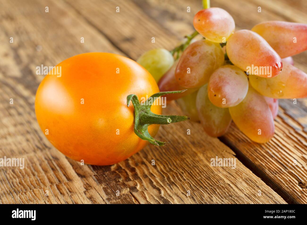 Close-up yellow tomato and bunch of grapes on wooden background. Shallow depth of field. Stock Photo