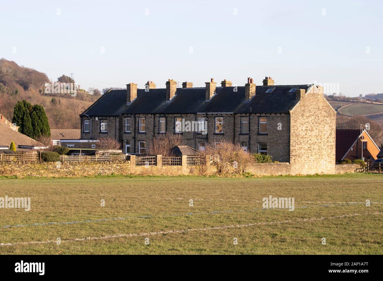 A series of typical Yorkshire stone built terraced houses with chimneys adjacent to a grass field in Huddersfield, West Yorkshire, U.K. Stock Photo