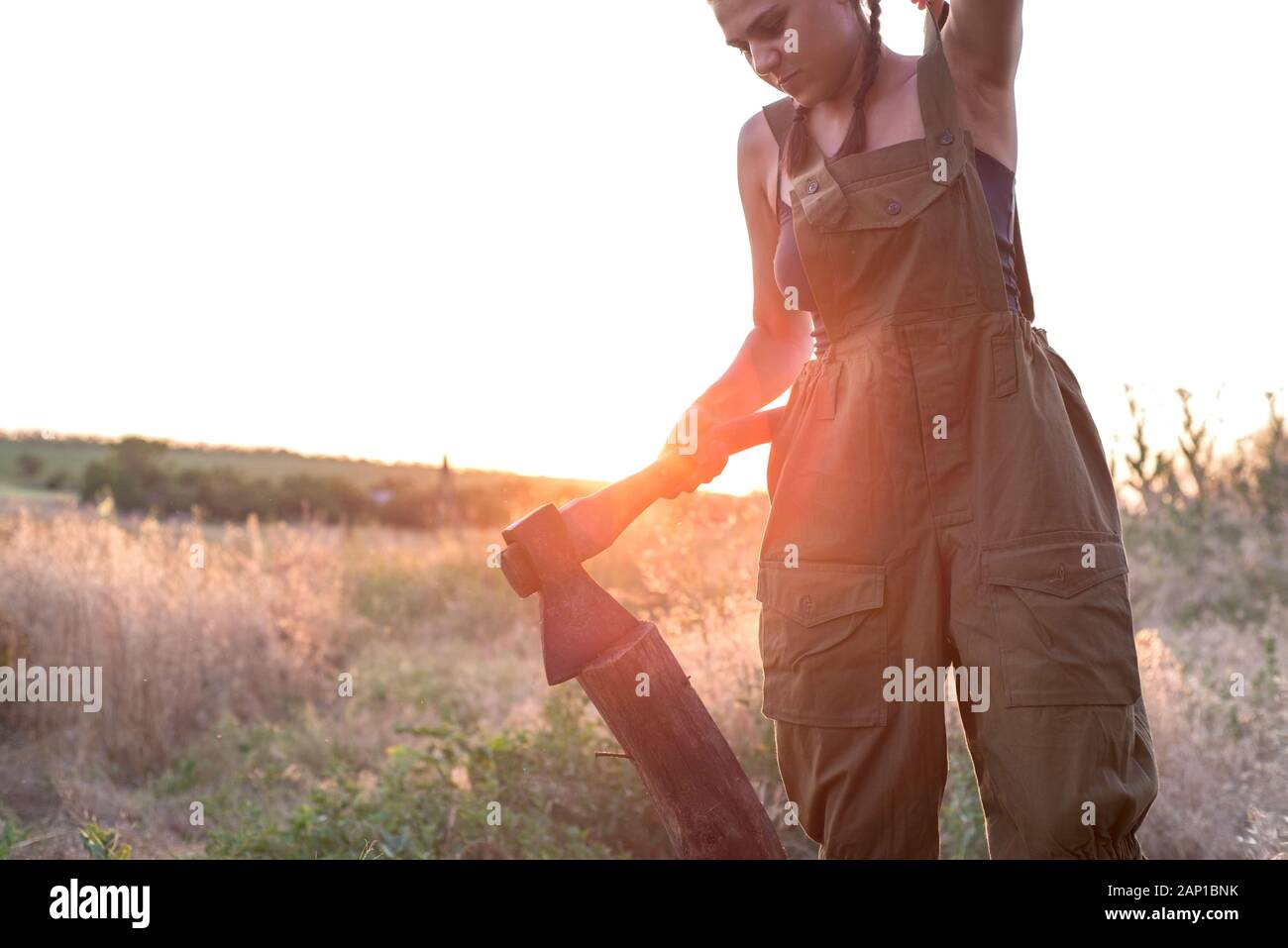 portrait of a beautiful young model girl. In working equipment, a woman works with an ax, waves, stands in a field. Country style Stock Photo