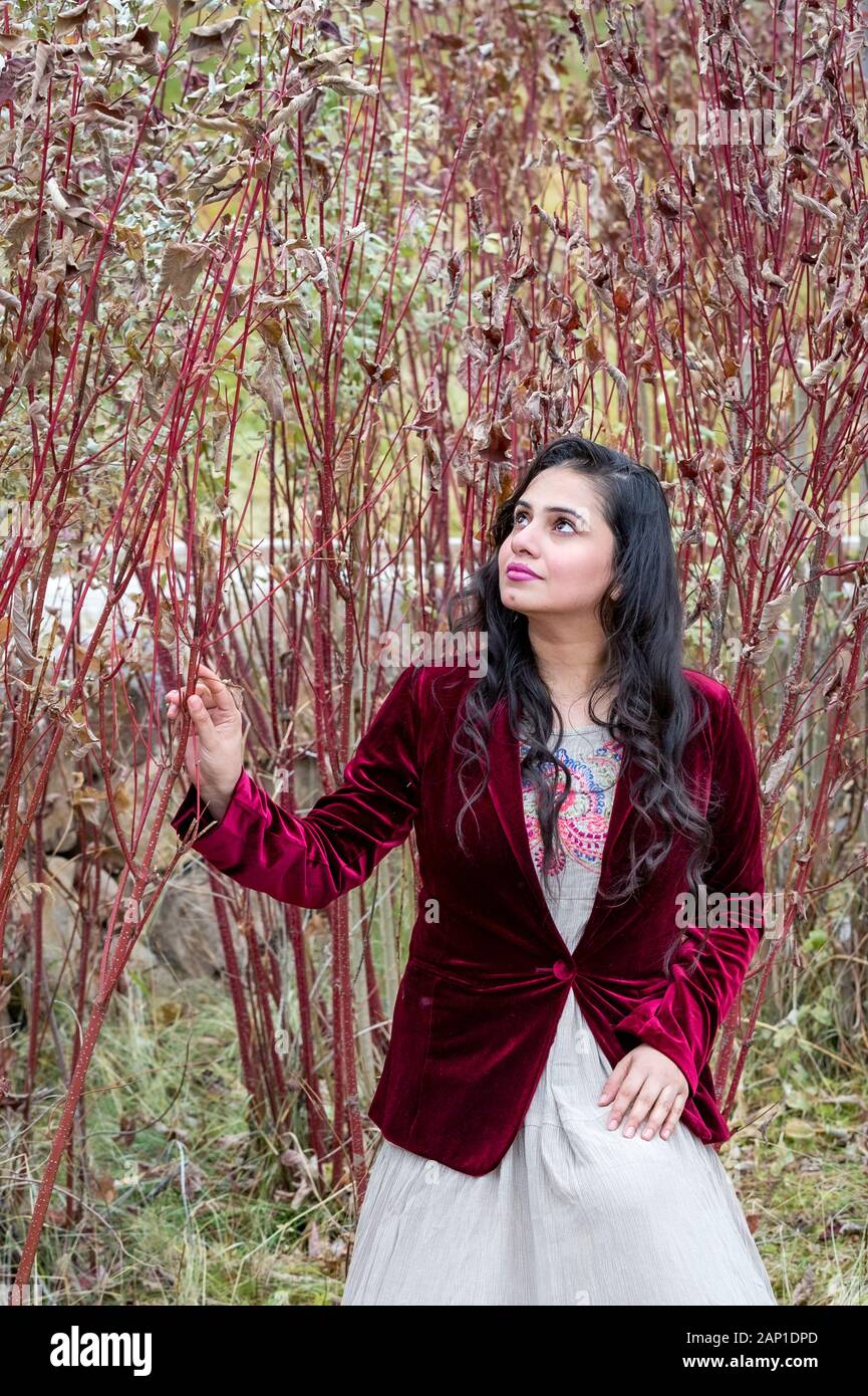 Beautiful young woman in red jacket standing by red bush Stock Photo