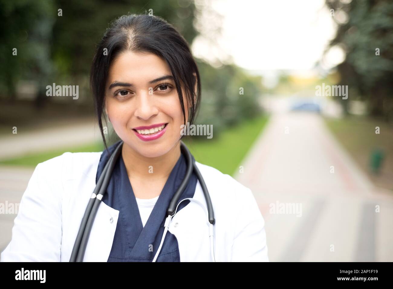 portrait of a beautiful, young mexican girl doctor. Smiles. Woman in a white coat with a stethoscope. Outdoor in Stock Photo
