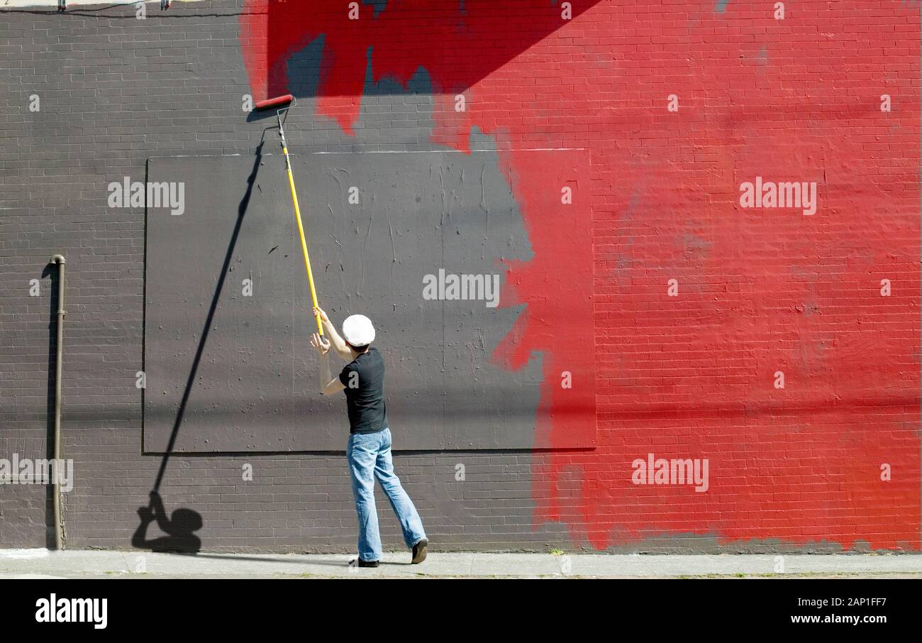 Handyman halfway through painting a gray wall with red paint using a