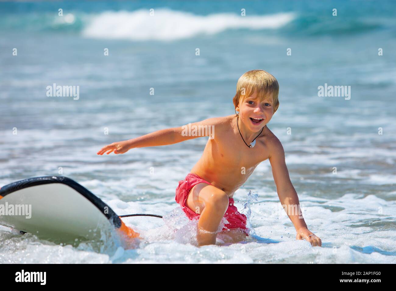 Happy boy - young surfer learning ride, jump from surfboard, run to beach. Active family lifestyle. Kids surf lessons, outdoor water sport activity Stock Photo