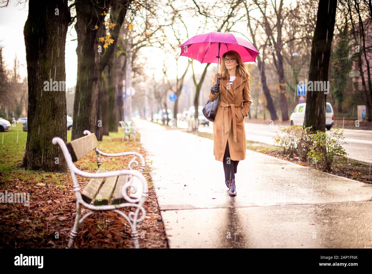 Full length shot of mature woman holding umbrella while walking on the street on a rainy day. Stock Photo