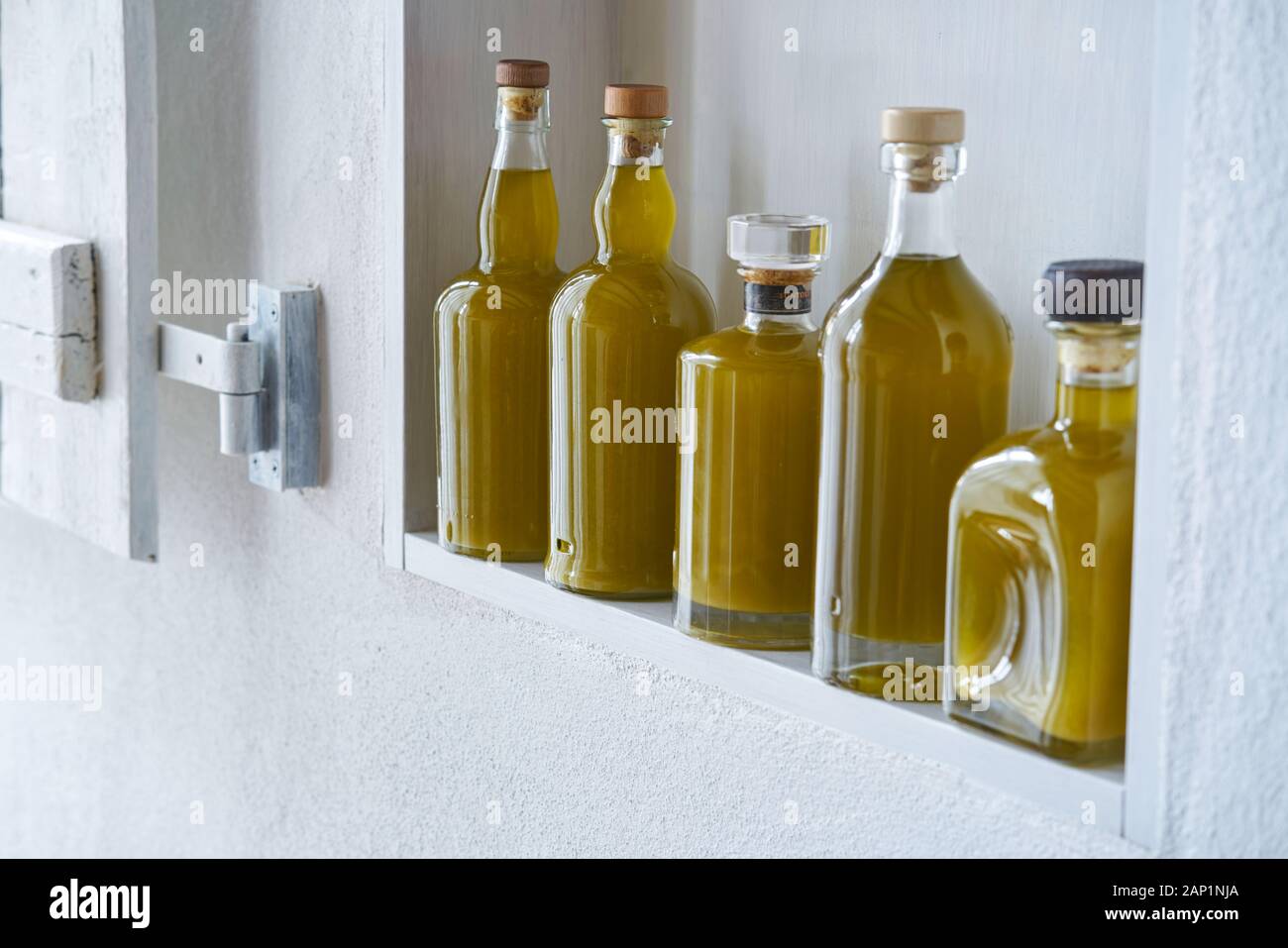 five bottles organic fresh healthy olive oil standing in a shelf in a country style house, gold yellow color and ambiance mood Stock Photo