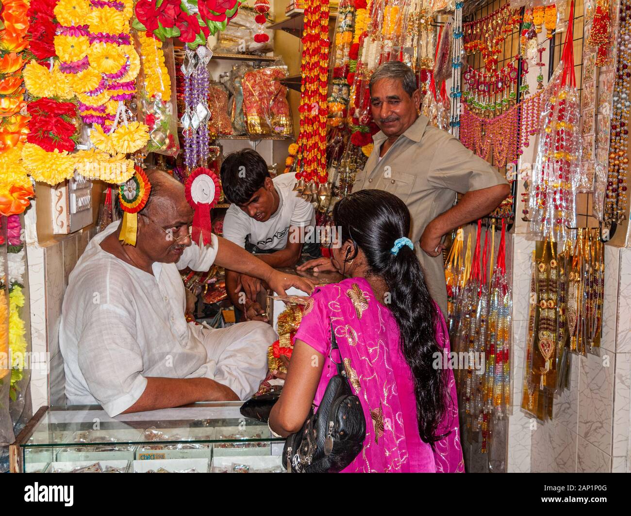 A vendor is selling artificial flowers and garlands in a colorful  shop Stock Photo
