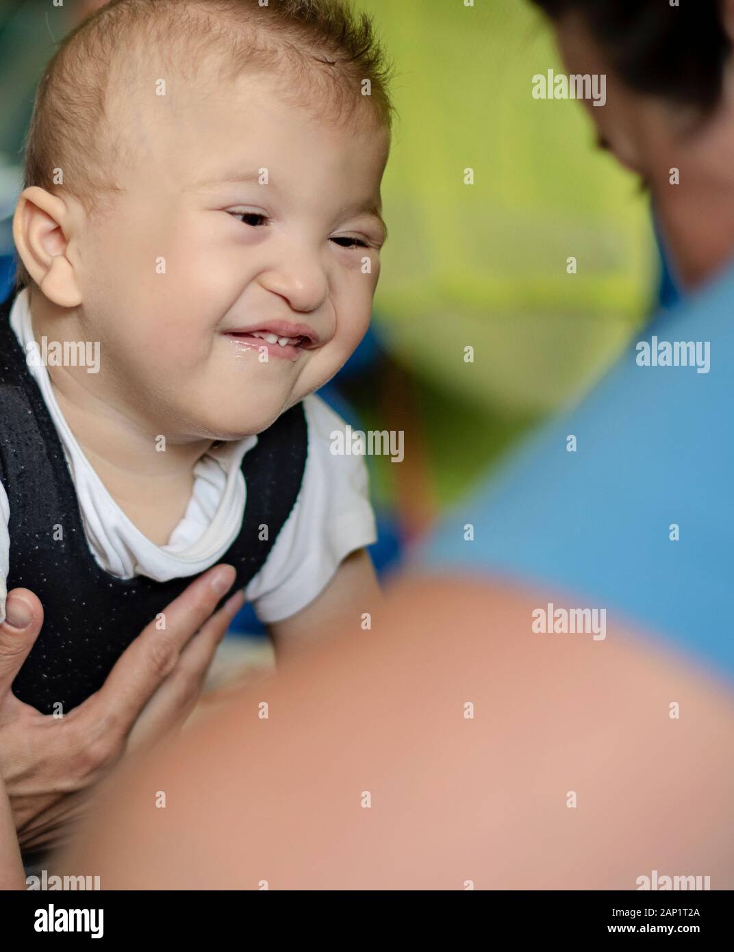 Portrait of a smiling baby with cerebral palsy on physiotherapy in a children therapy center. Boy with disability has therapy by doing exercises. Stock Photo