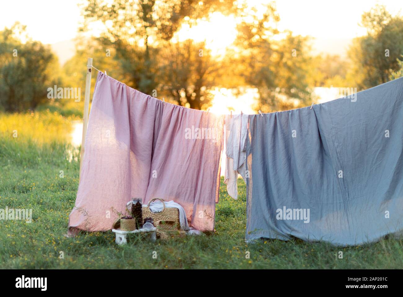 Pink and blue bedding sheet on forest background under the bright warm sun. Clean bed sheet hanging on clothesline at backyard. Hygiene sleeping ware concept. Stock Photo