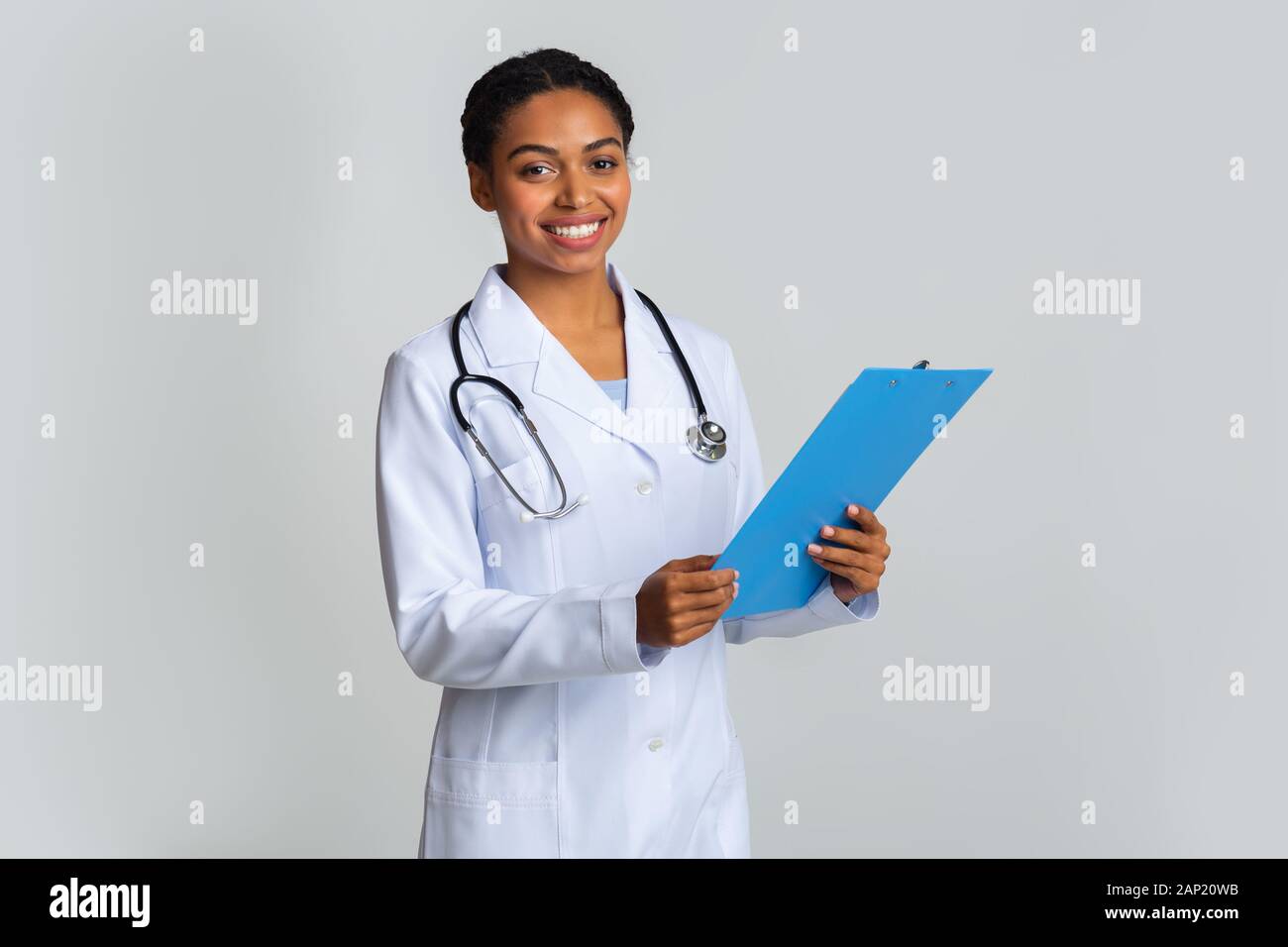 Young afro female doctor in white coat with clipboard in hands Stock Photo