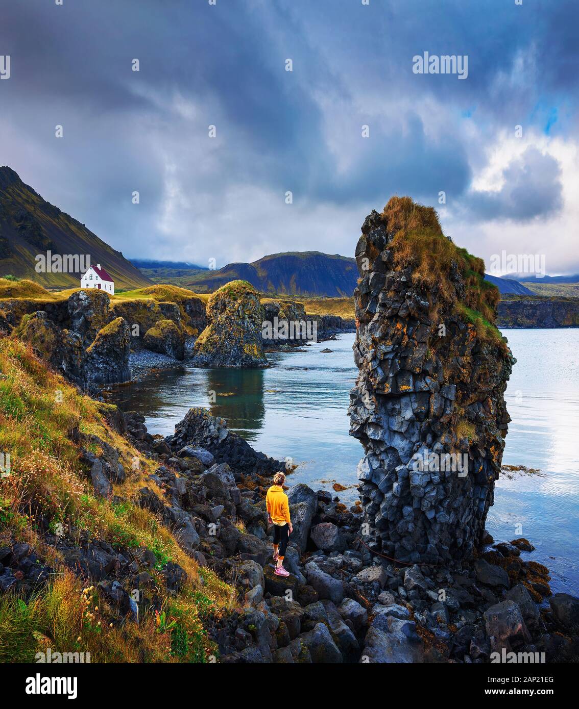 Tourist on a rocky beach looks at a small house in Arnarstapi, Iceland Stock Photo