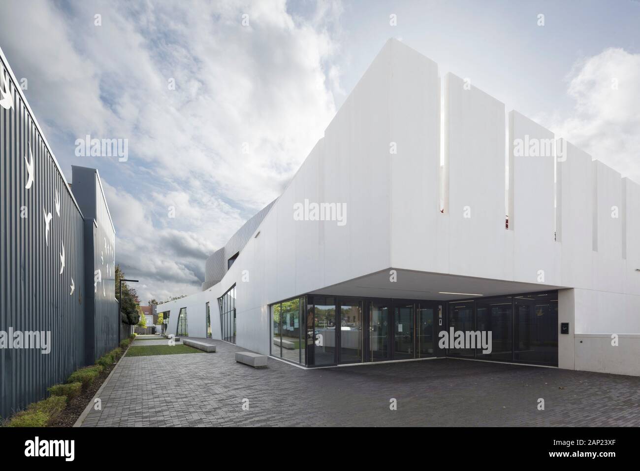 View of secondary entrance against afternoon sky. Cultuurcentrum De Factorij, Zaventem, Belgium. Architect: ebtca Architecten & Archiles architecten , Stock Photo