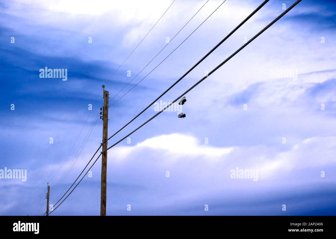 A pair of sneakers dangling on power lines under a cloudy blue sky, a metaphor for desertion and abandonment Stock Photo