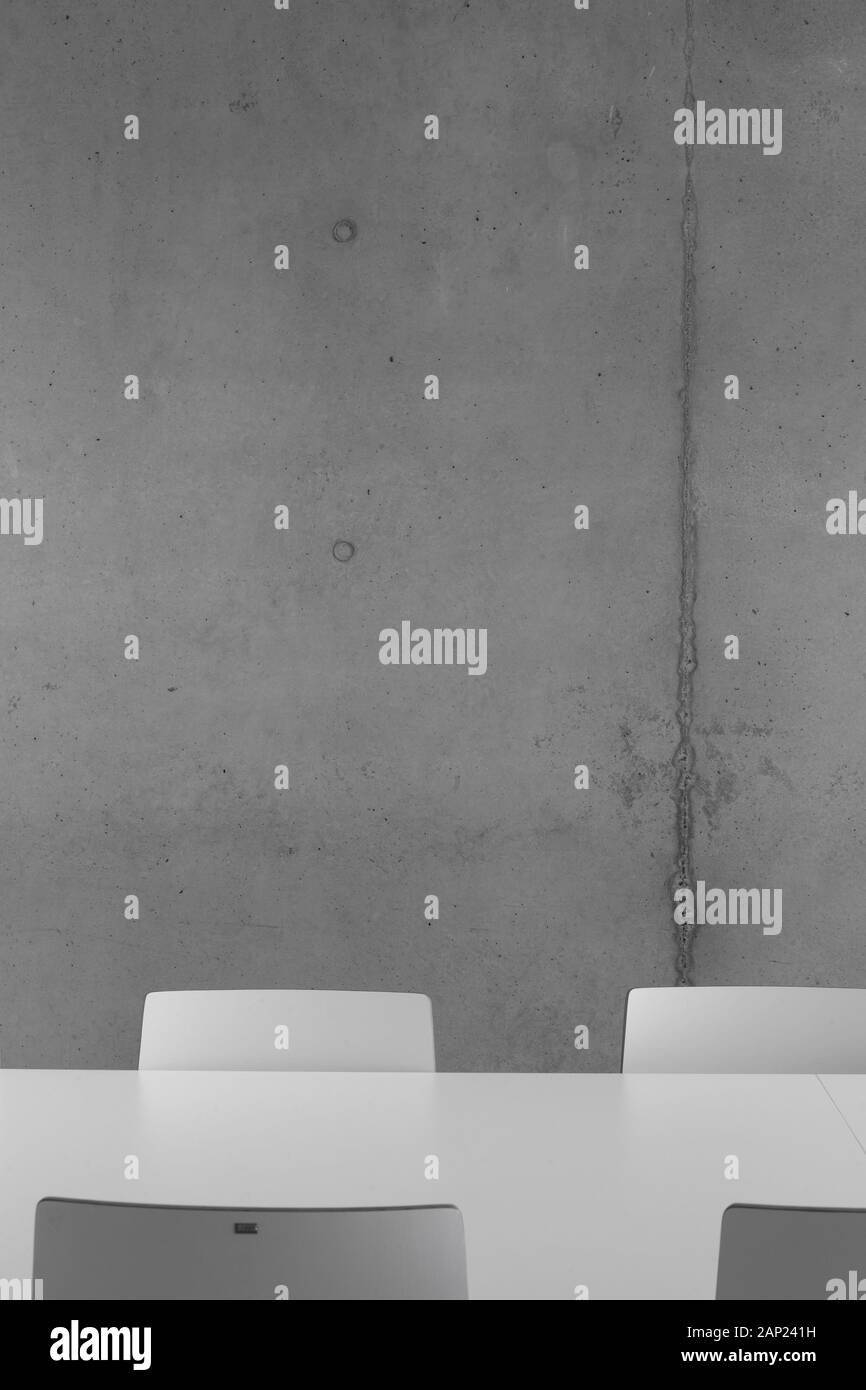 Detail of white table and chairs against concrete wall in meeting room. Cultuurcentrum De Factorij, Zaventem, Belgium. Architect: ebtca Architecten & Stock Photo