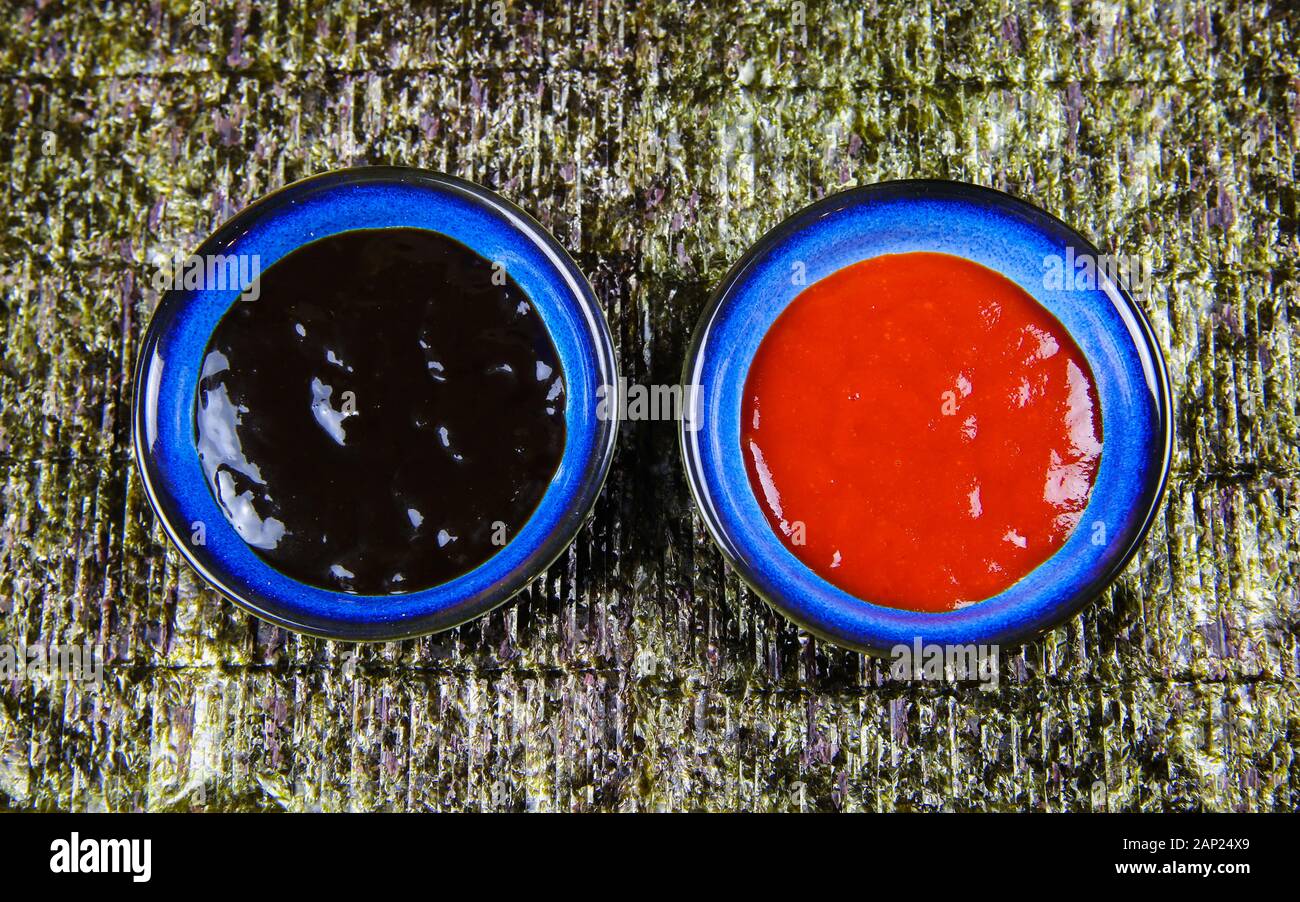 Two bowls with black hoi sin and red hot spicy chili sauce on nori