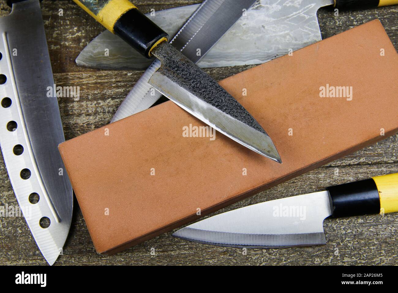 Grinding knifes: Close up of different metal japanese kitchen knifes with sharpening stone on wood table Stock Photo