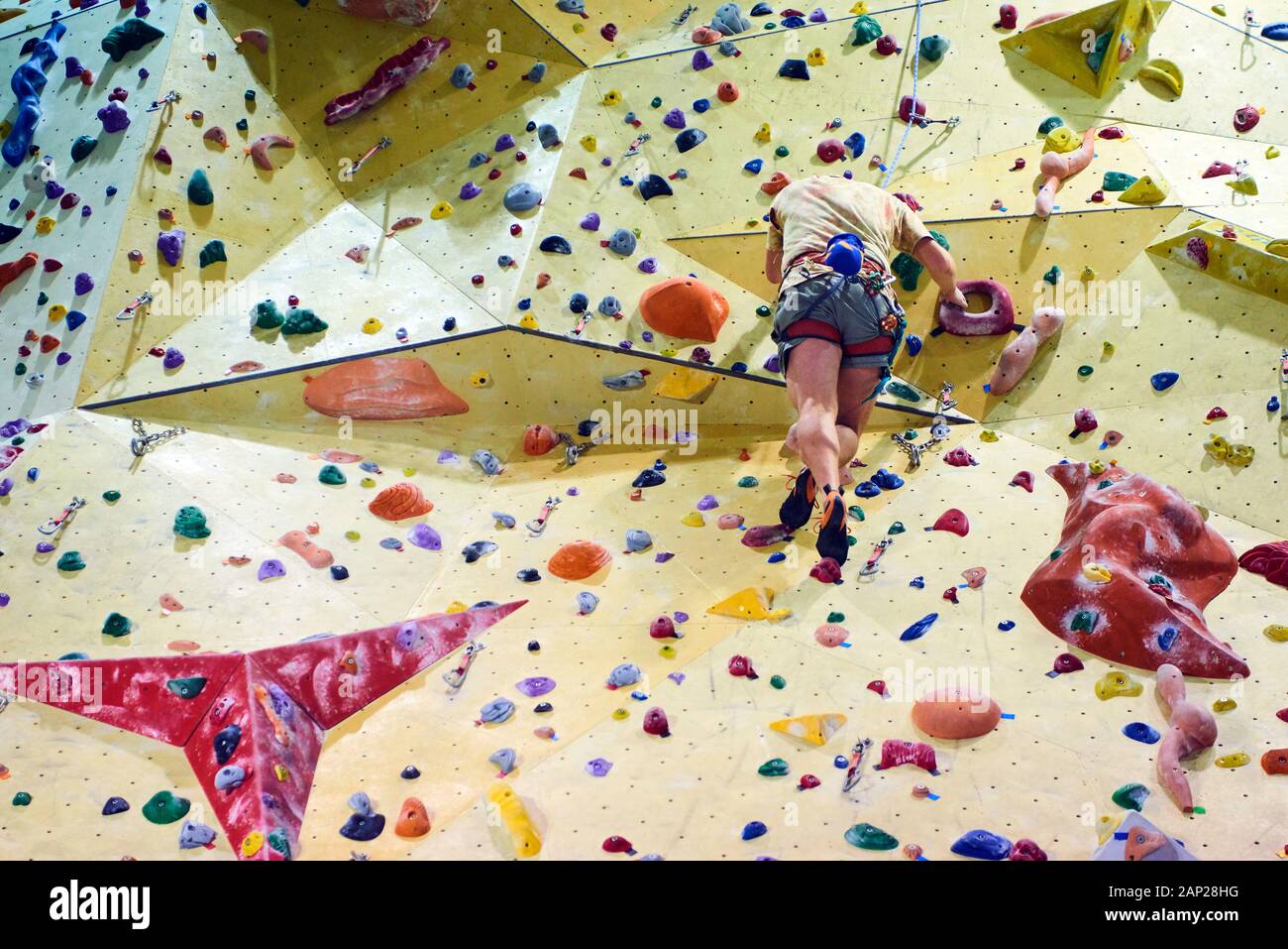 Man climbing wall in bouldering gym. Detail on legs and equipment Stock