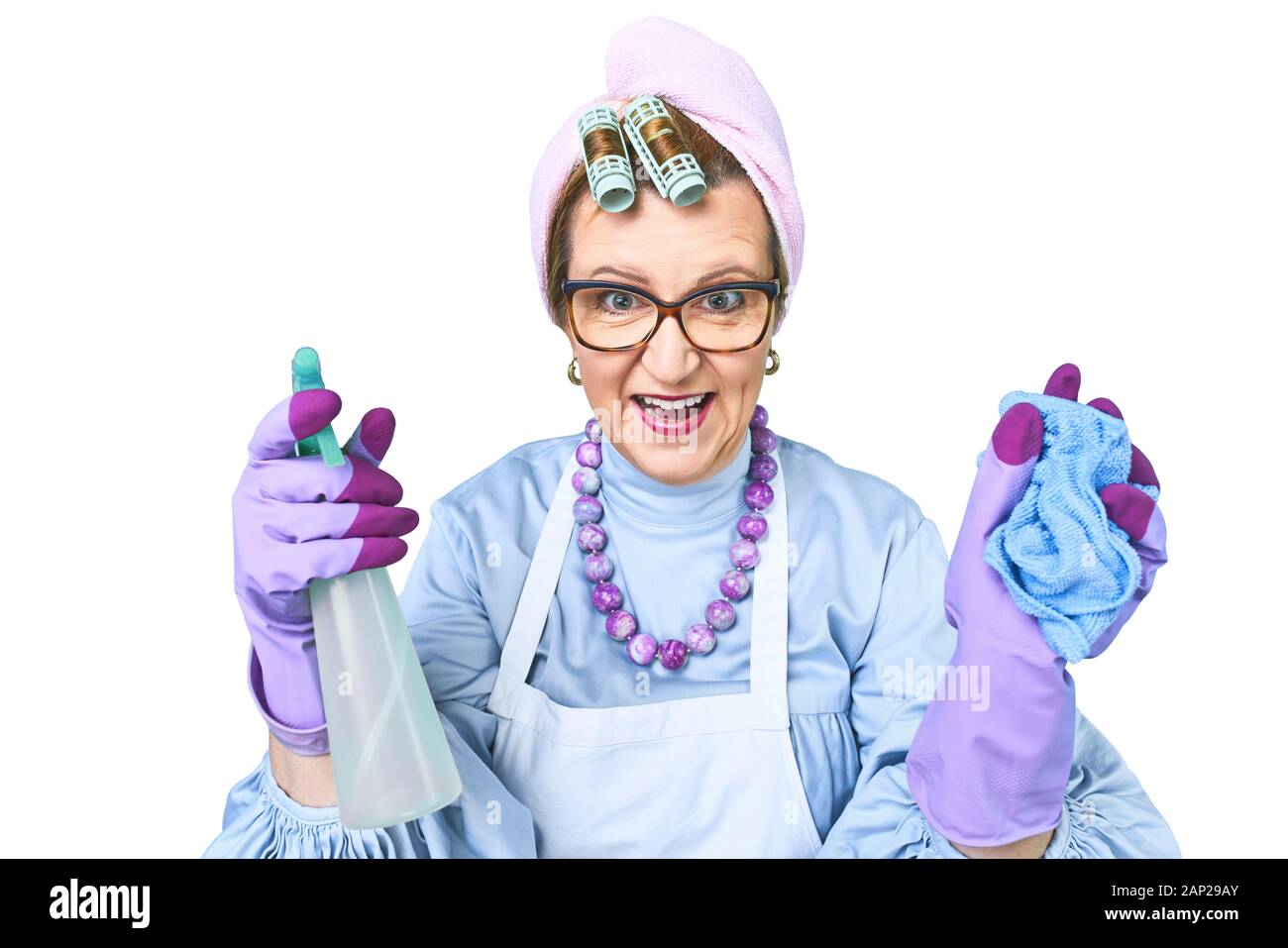 Portrait of happy old cleaning woman in apron with dust cleaning brush isolated on blue background. special uniform and professional equipment for Stock Photo