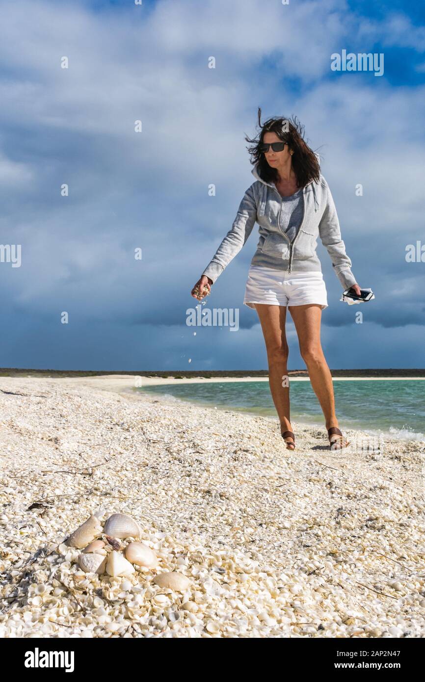 Low perspective image of female tourist with handful of falling cockle shells on Shelkl Beach at Shark Bay in Western Australia. Stock Photo