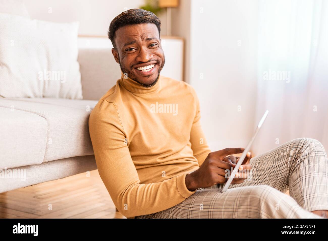 Afro Man Using Tablet Smiling Sitting On Floor At Home Stock Photo