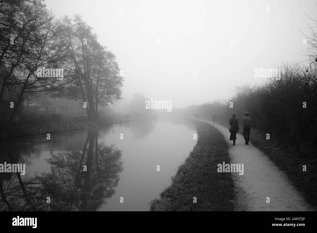Early misty morning by the Trent and Mersey canal (Staffordshire,UK). Couple walks on the footpath that goes in to eternity Stock Photo